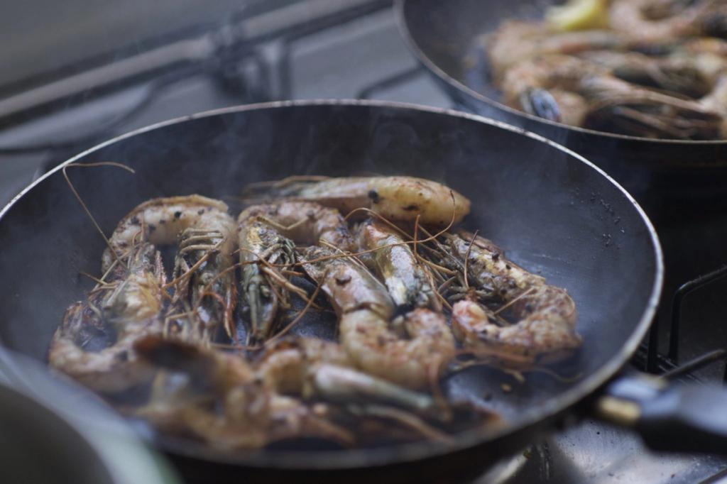 Креветки и морепродукты, жарящиеся на сковородах