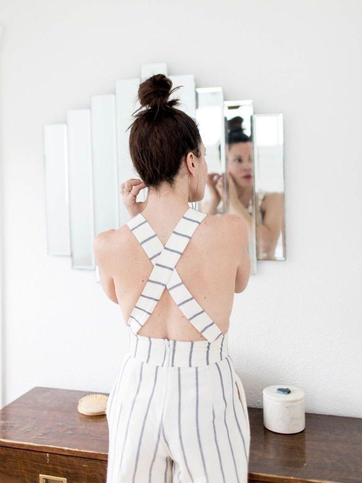 A woman seen from behind at a mirror, wearing a striped Tribe Alive jumpsuit with crossover straps