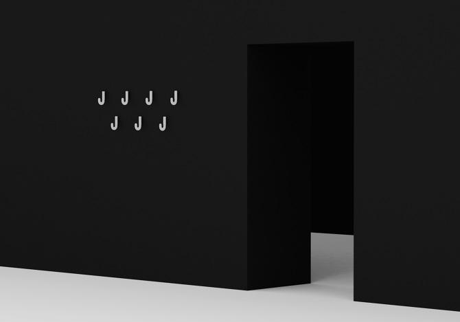 Seven white J-shaped wall hooks on a black wall beside a doorway, designed by Maxim Maximov