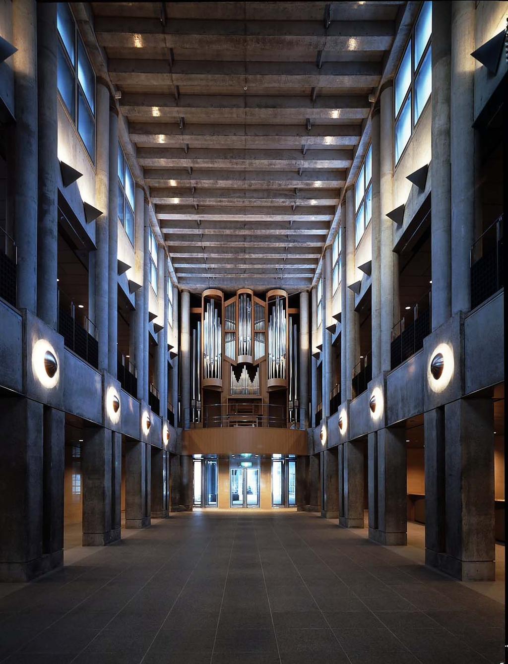 Interior of the Art Tower Mito concert hall: a tall concrete volume with an organ at the far end, symmetrical rows of columns and circular wall-mounted light fixtures