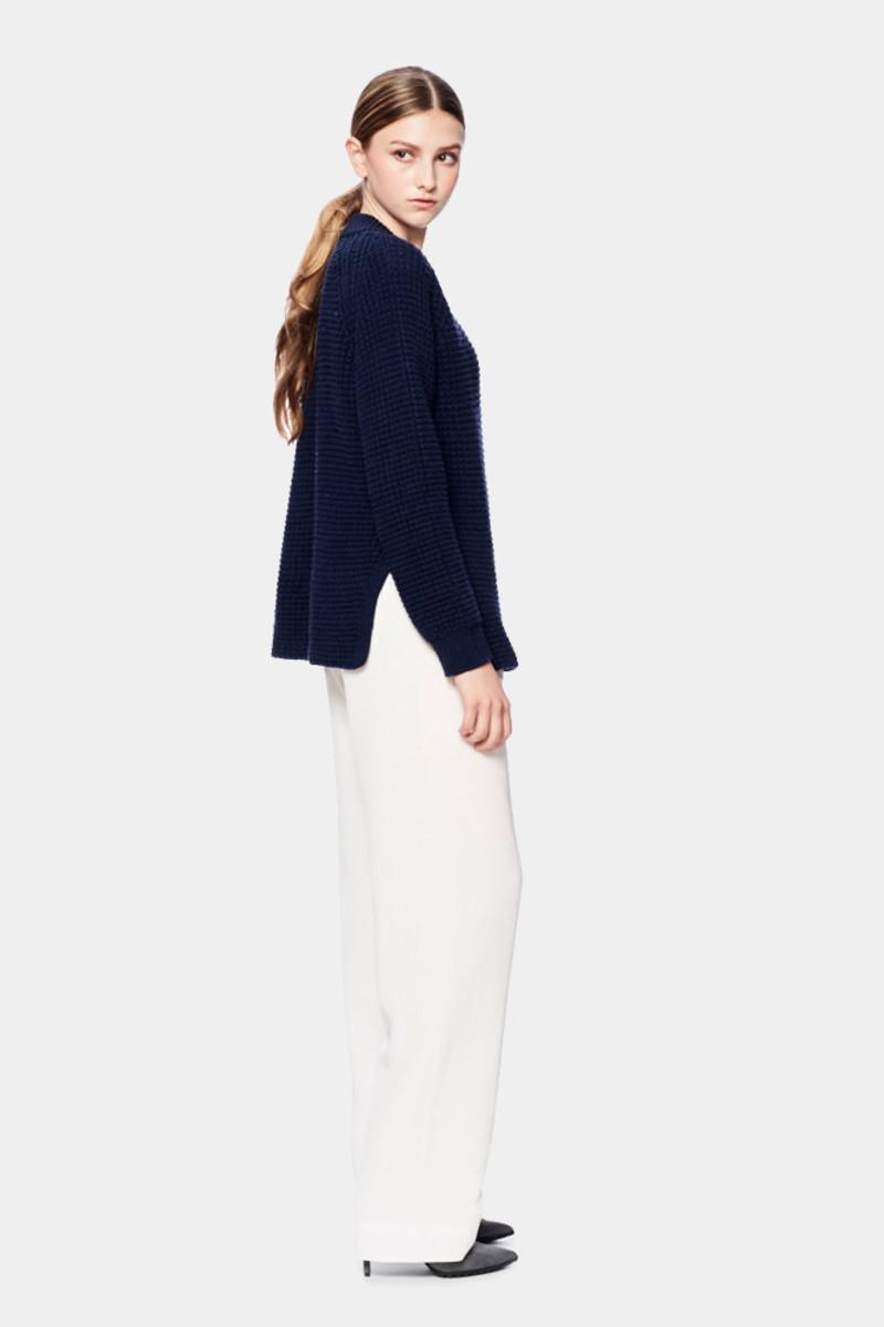 A model seen from behind in a dark navy knitted sweater and wide white trousers