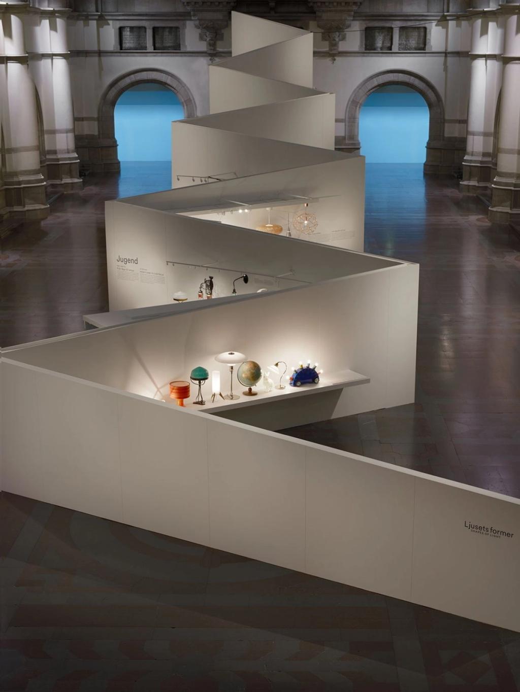 An exhibition hall with white zigzag display stands and illuminated light fixtures
