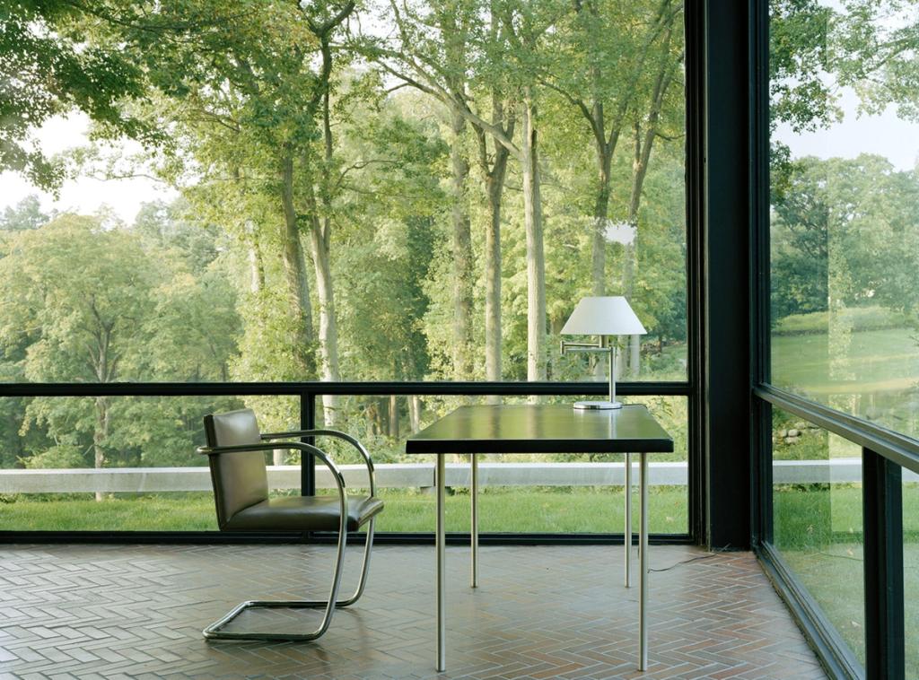 Philip Johnson's Glass House: a Brno table and chair beside the transparent wall overlooking the greenery
