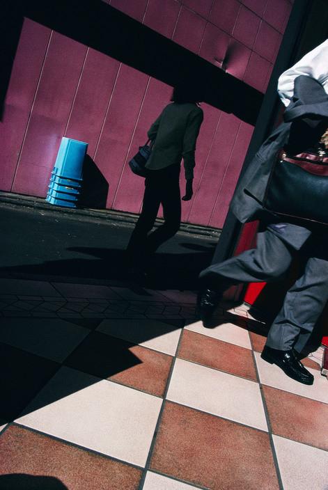 The silhouette of a passer-by against a purple wall and tiled floor in harsh light