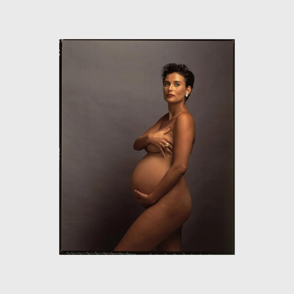 A nude, pregnant Demi Moore in profile against a dark background