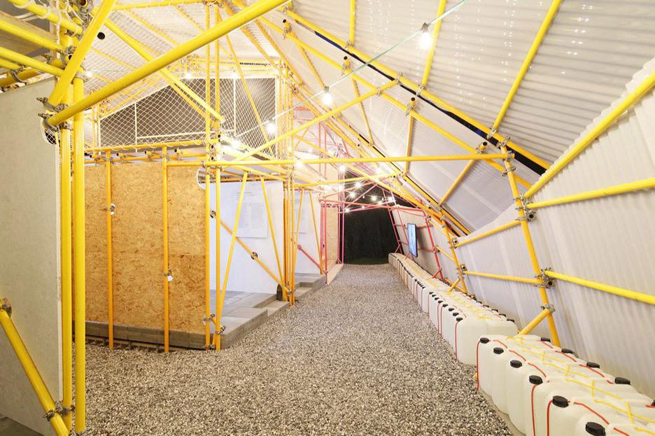 Interior of Kibera School: yellow tubular columns, a gravel floor and a row of white canisters along the wall