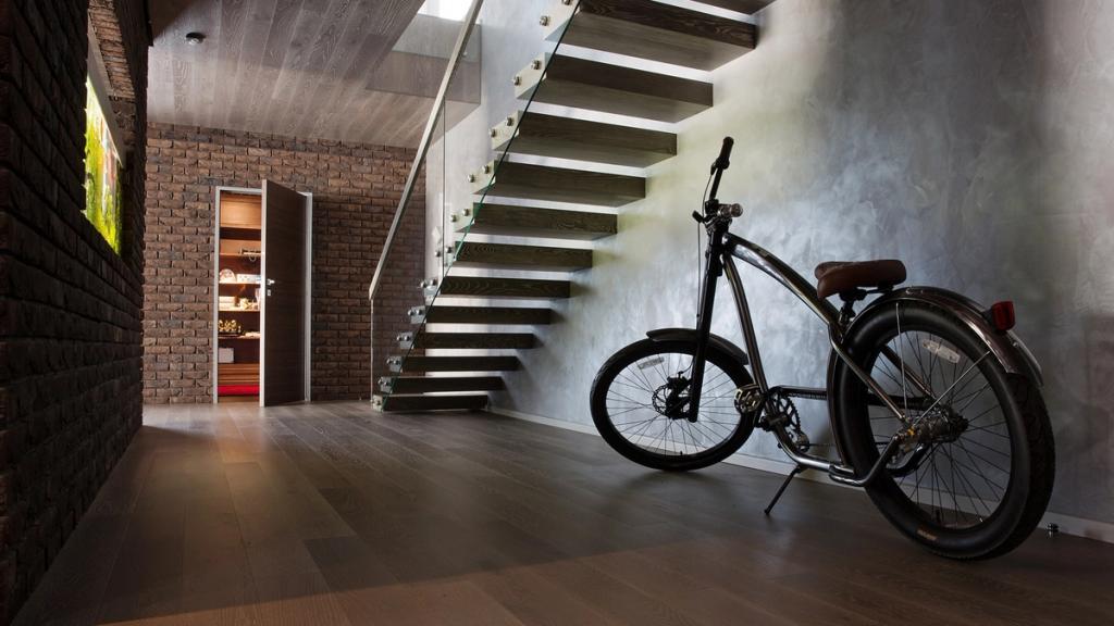 A hallway with a floating staircase on a glass balustrade and a bicycle propped against a concrete wall