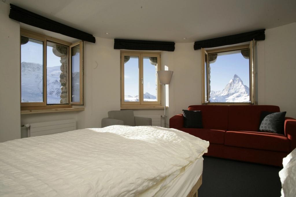 A room with a white bed and red sofa, the Matterhorn framed in the windows