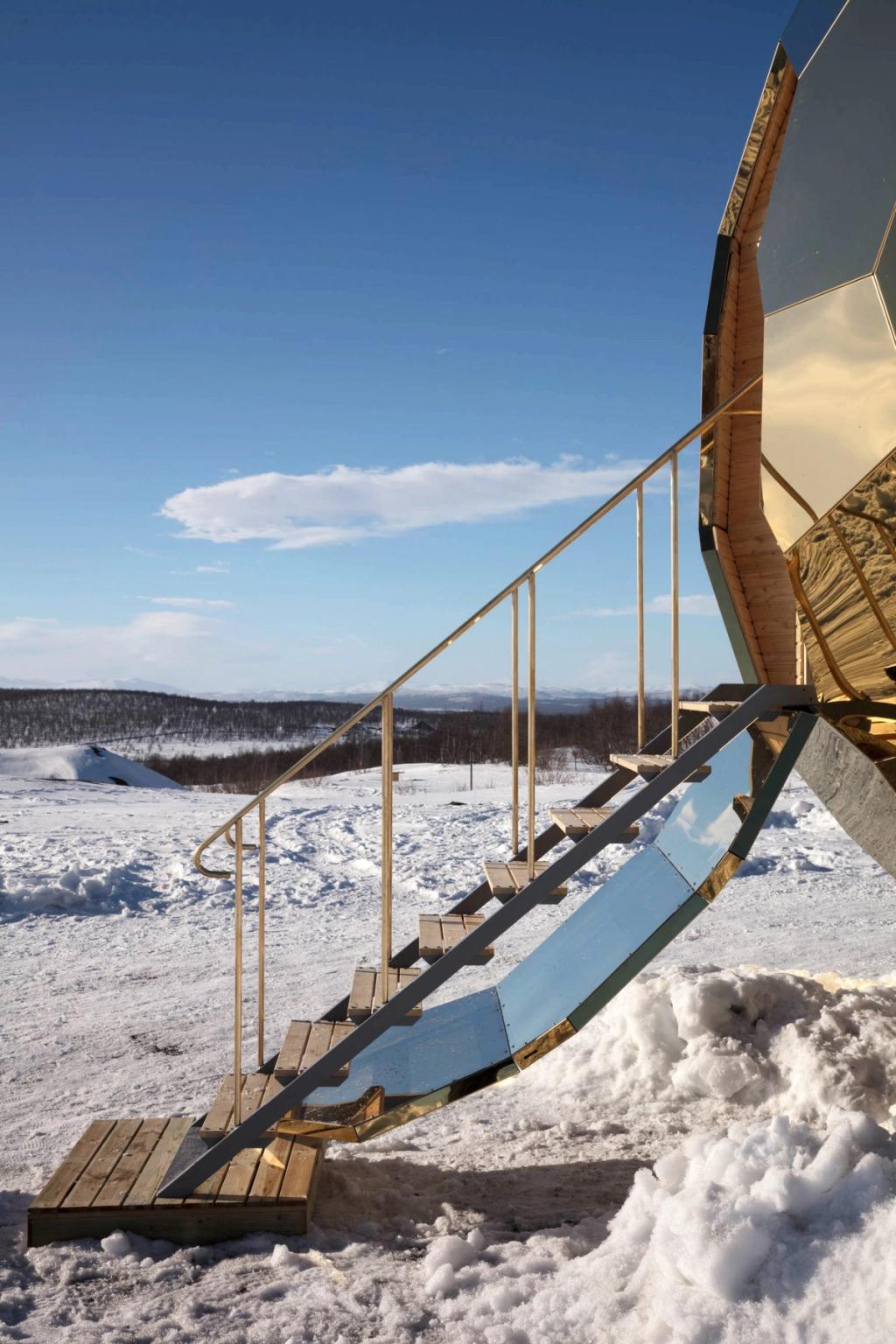 The staircase leading to the entrance of the golden Solar Egg sauna, with a panoramic view of snow-capped mountains
