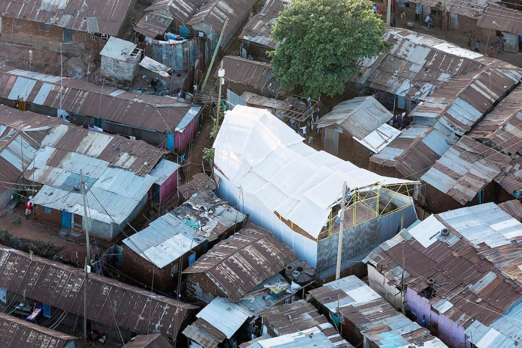 Kibera School: a bright structure with a translucent roof rising above the rusted rooftops of the slum, aerial view