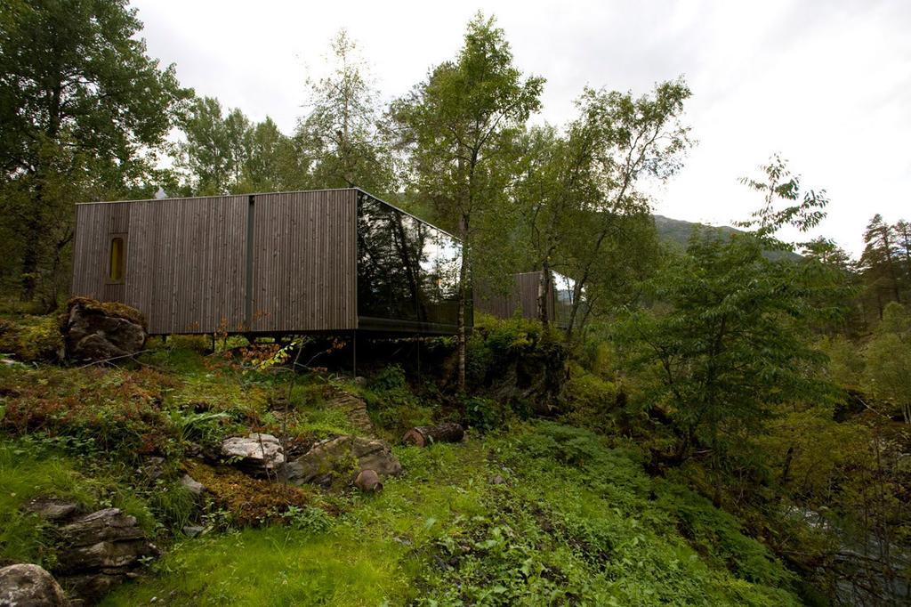 Деревянный домик Juvet Landscape Hotel со стеклянной стеной среди берёз летом, Норвегия