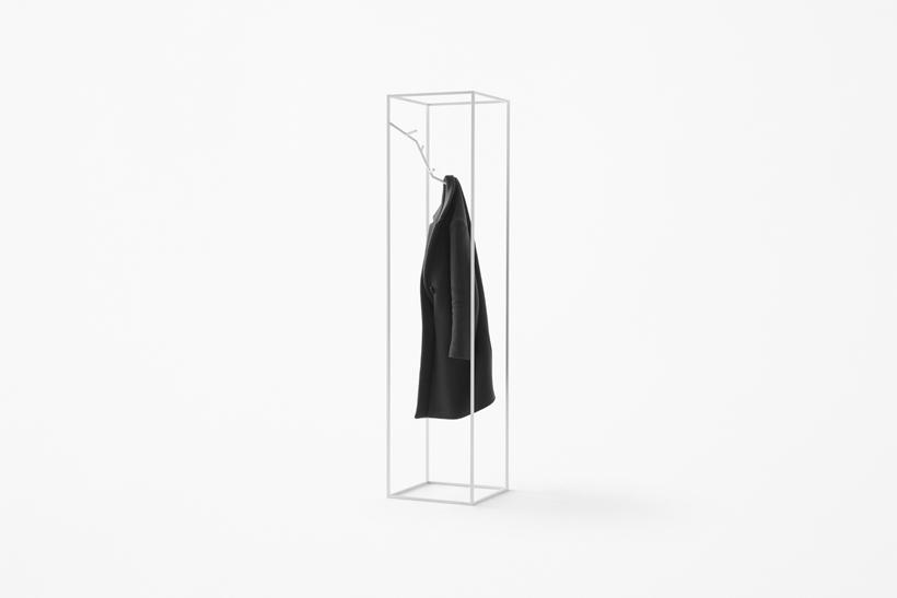A black coat on a minimalist white frame coat rack in the shape of a rectangular prism