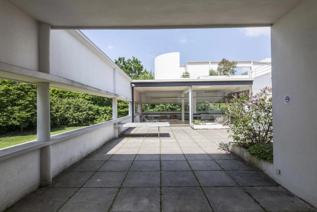 The terrace of Villa Savoye with a window opening onto greenery and a tiled floor