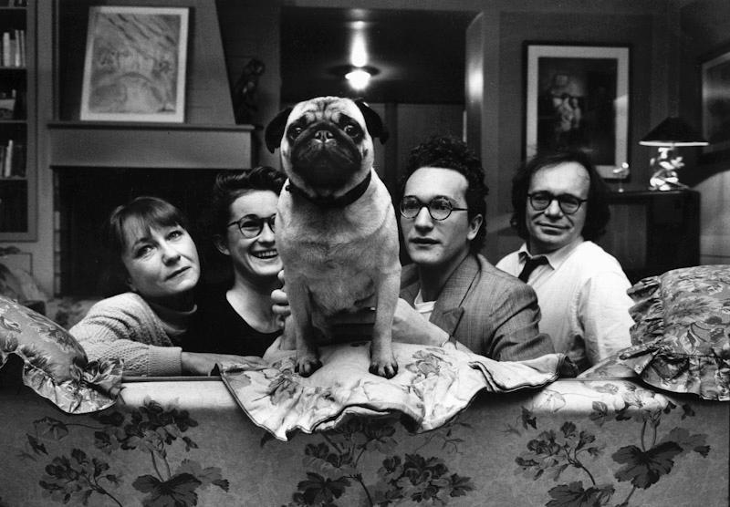 A pug stands on the back of a sofa, flanked by four people wearing glasses