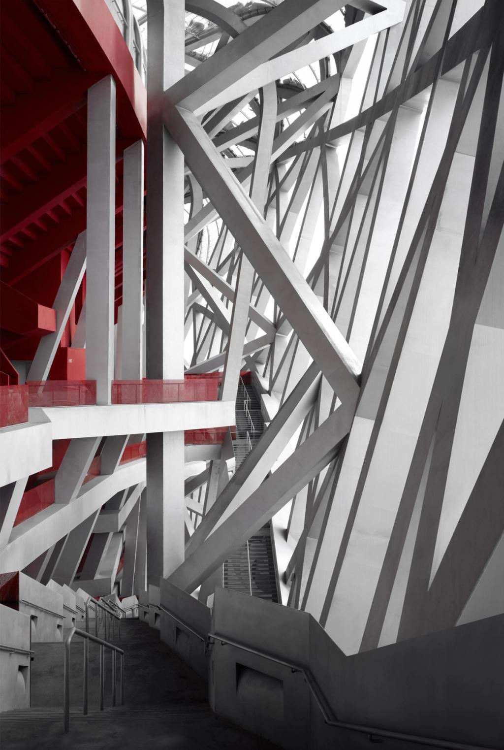 The interior load-bearing structure of a stadium: an interlacing of grey steel beams with red accents