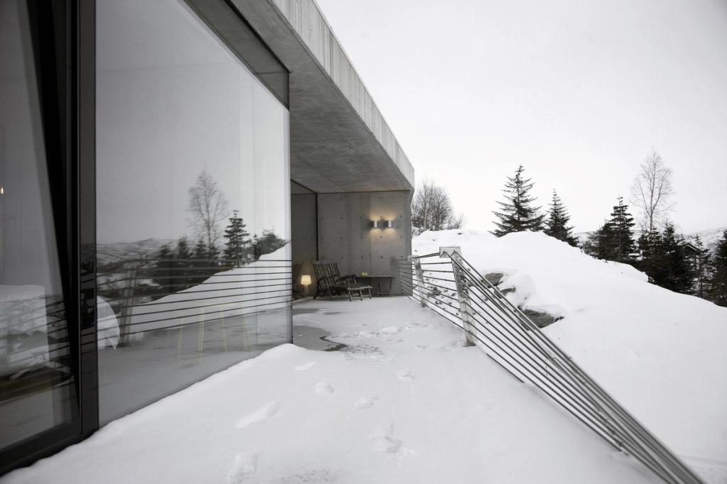 A concrete house with mirror glazing set on a snowy slope among fir trees