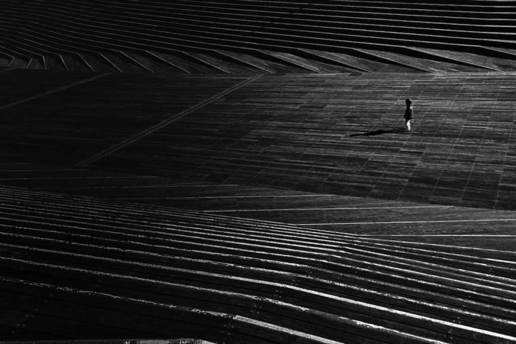 A tiny human figure is lost among the broad, dark steps of an enormous staircase