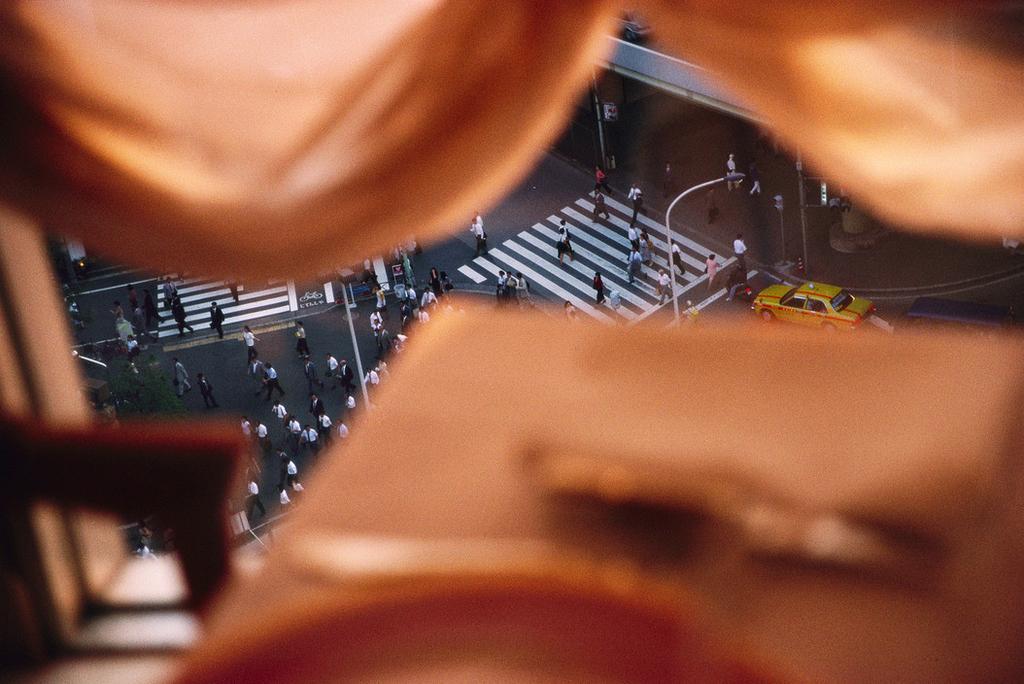 A Tokyo intersection with pedestrians and a yellow taxi, shot from above through lens flare
