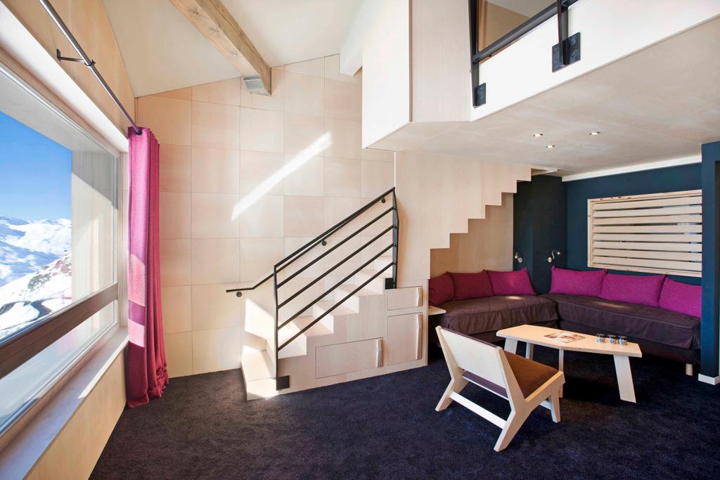 A two-level hotel room with a staircase, a fuchsia sofa and a mountain-view window