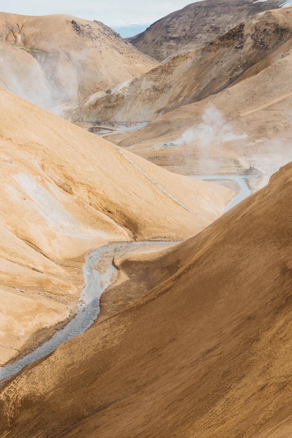 The ochre mountains of Kerlingarfjöll with a trail and stream in the valley, wisps of steam rising from geothermal springs