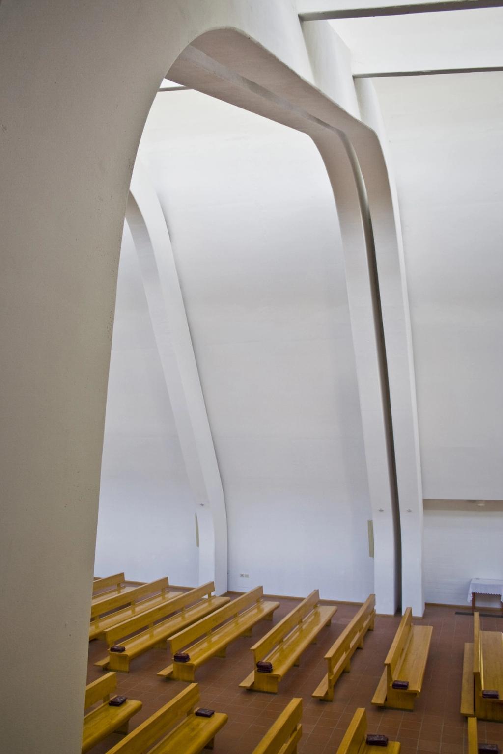 Interior of Riola Church with white asymmetrical concrete arches and wooden pews
