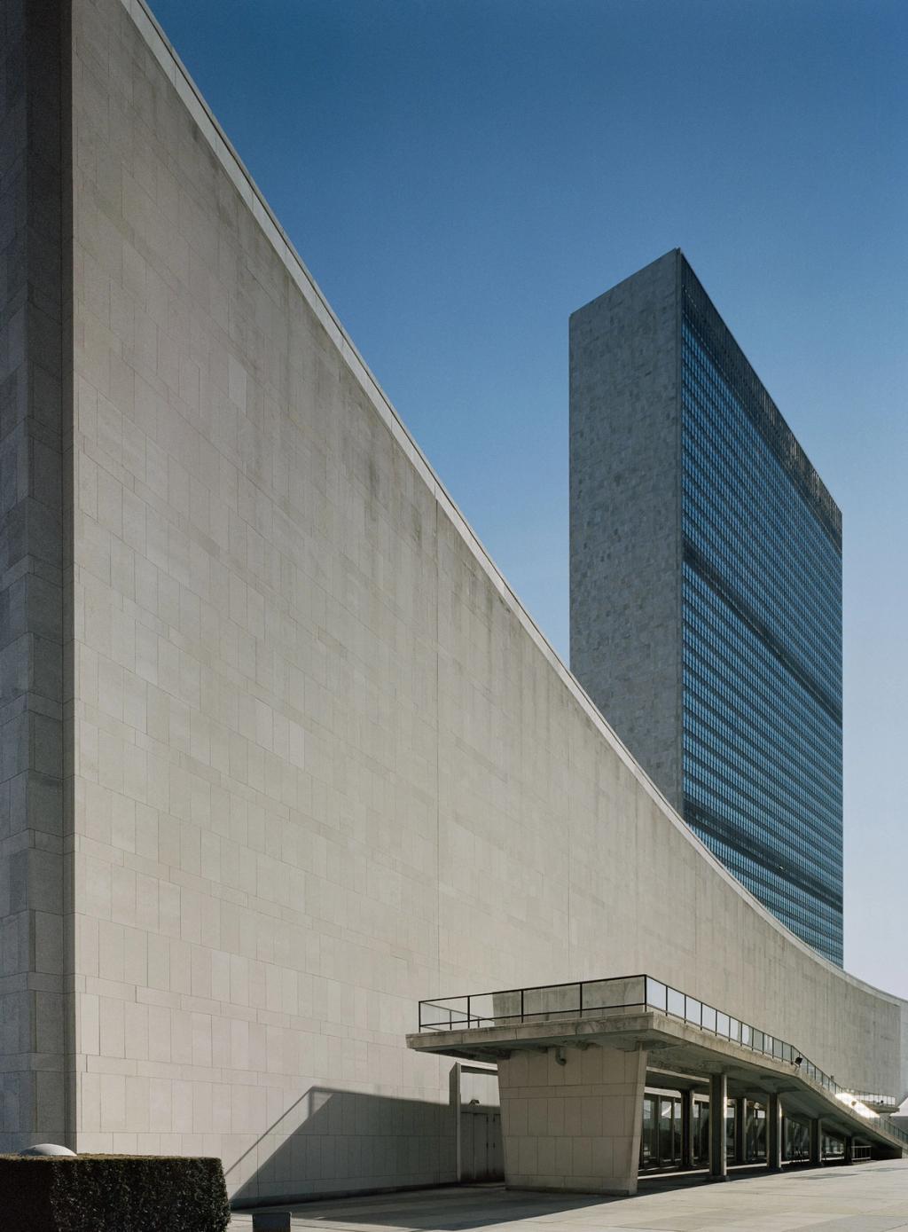 The curved wall and glass tower of the UN Headquarters in New York against an open sky