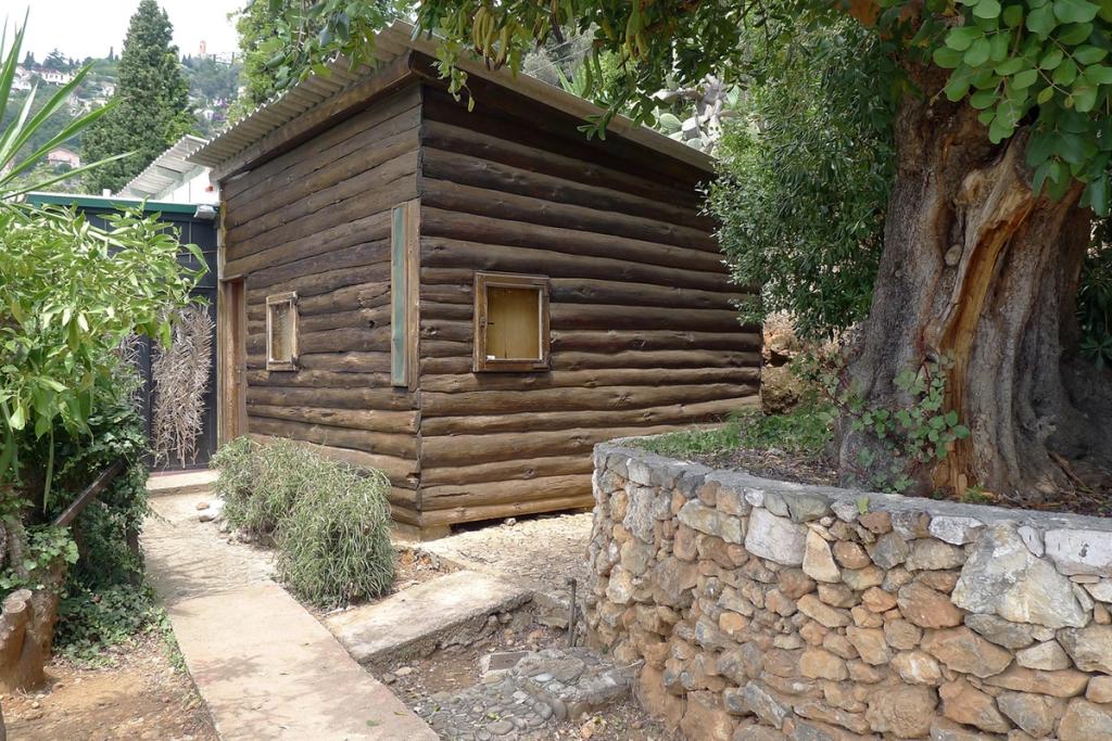 Le Corbusier's log Cabanon against a stone wall amid lush greenery