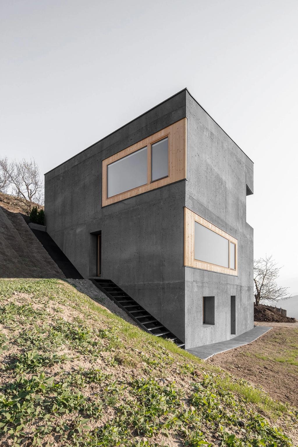The cubic concrete house by architect Andreas Gruber, with a staircase set into a hillside slope