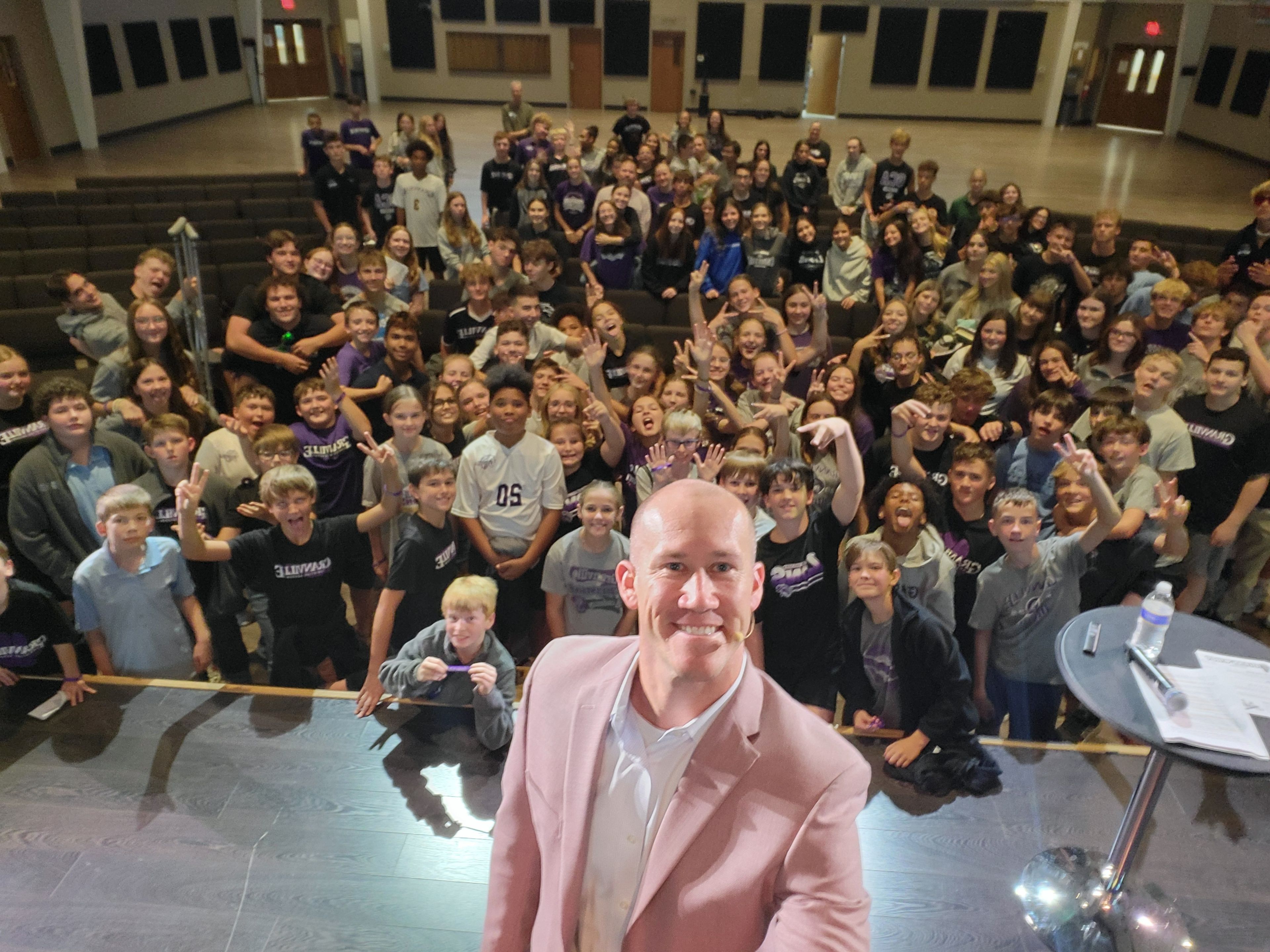 Taylor Candella taking an on-stage selfie with his audience of students.