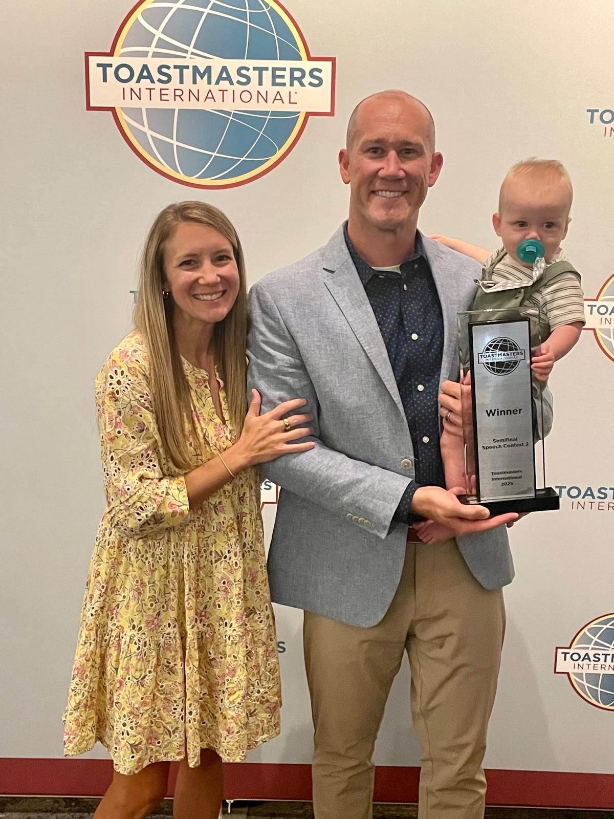 Taylor Candella and his family celebrating his Semifinal win at the 2025 Toastmasters World Championship, holding his first-place trophy.