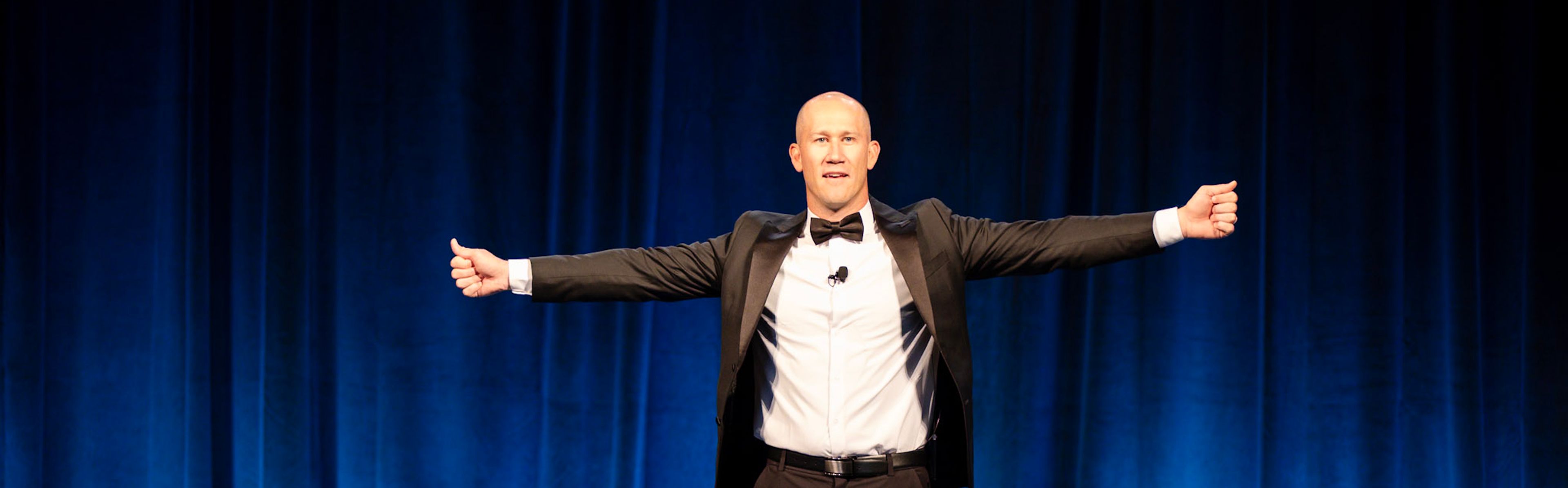 Taylor Candella delivering a keynote speech on stage, gesturing passionately to an audience.