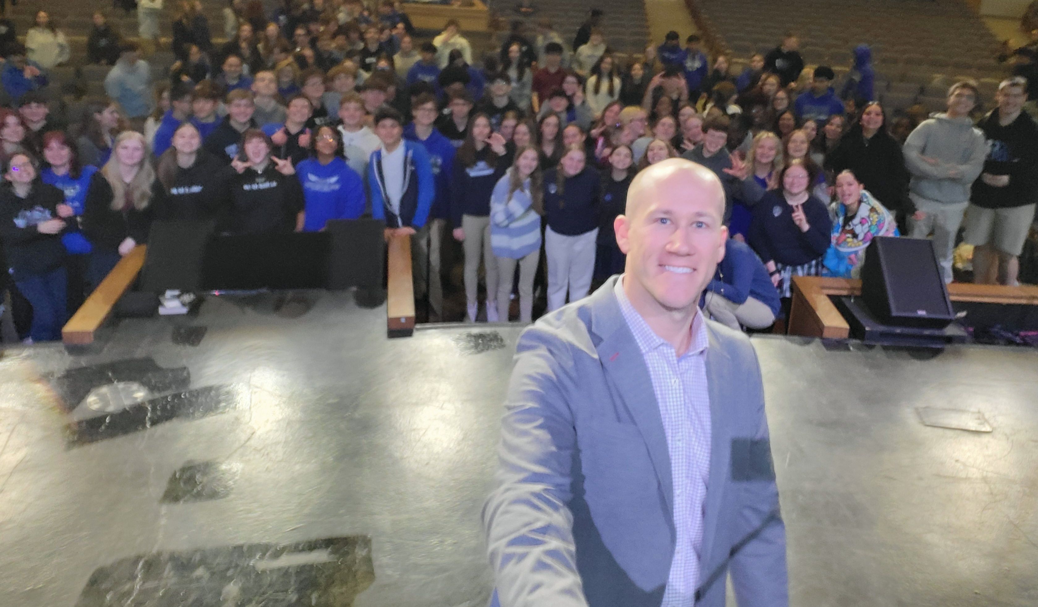 Taylor Candella taking an on-stage selfie with his audience of students.