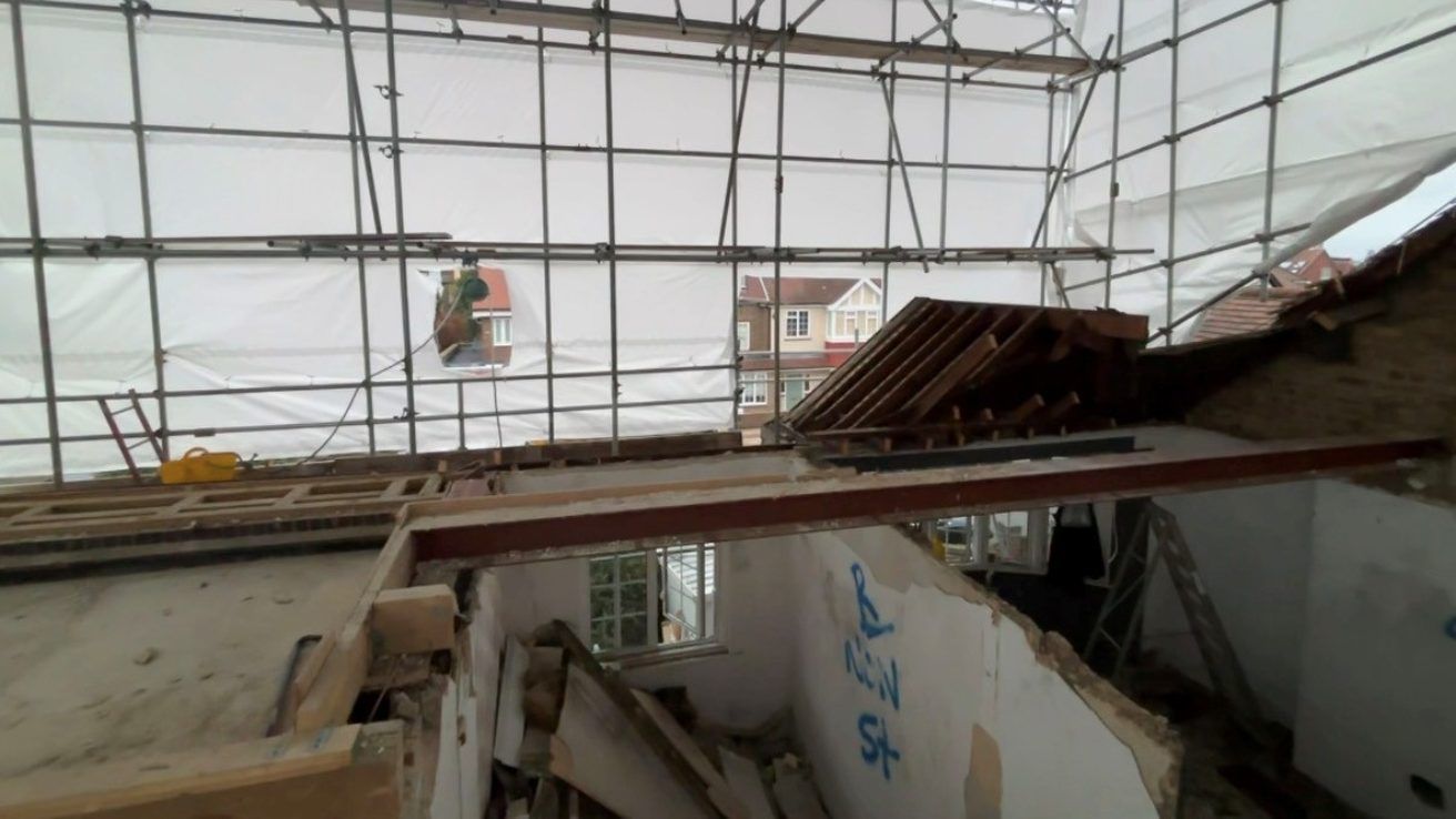 Roof removed and upper floor stripped inside a sheeted scaffold during demolition works in Chiswick.