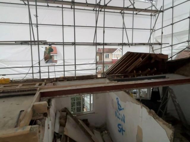 Roof removed and upper floor stripped inside a sheeted scaffold during demolition works in Chiswick.