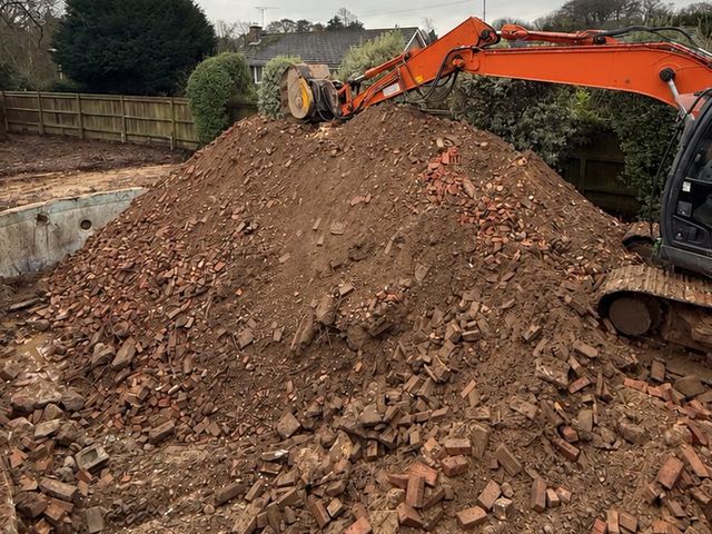 Tracked excavator working a mound of brick rubble and soil during site clearance in Portsmouth.