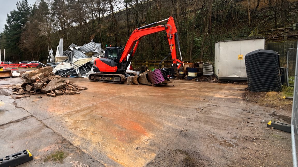 Tracked excavator beside the flattened steel sheeting of a demolished outbuilding in Byfleet, Surrey.