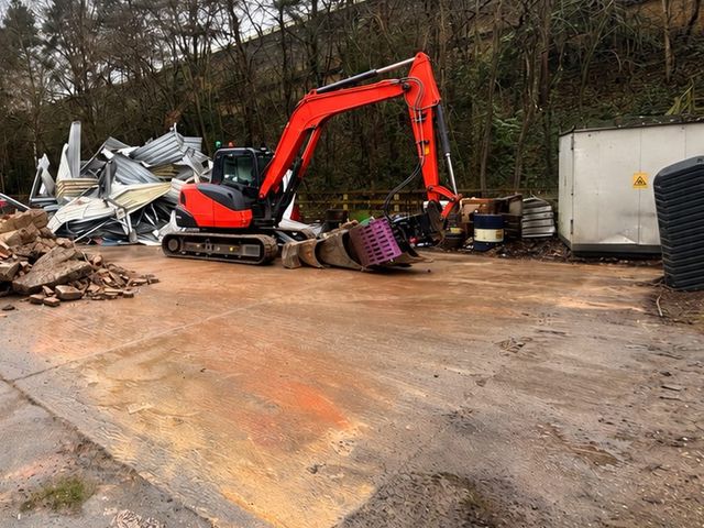 Tracked excavator beside the flattened steel sheeting of a demolished outbuilding in Byfleet, Surrey.