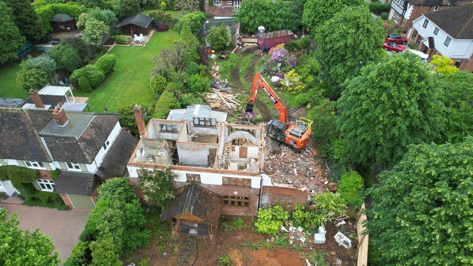 Aerial view of a house demolition in Esher with the roof removed and an excavator working at the rear of the plot