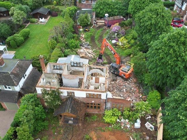 Aerial view of a house demolition in Esher with the roof removed and an excavator working at the rear of the plot