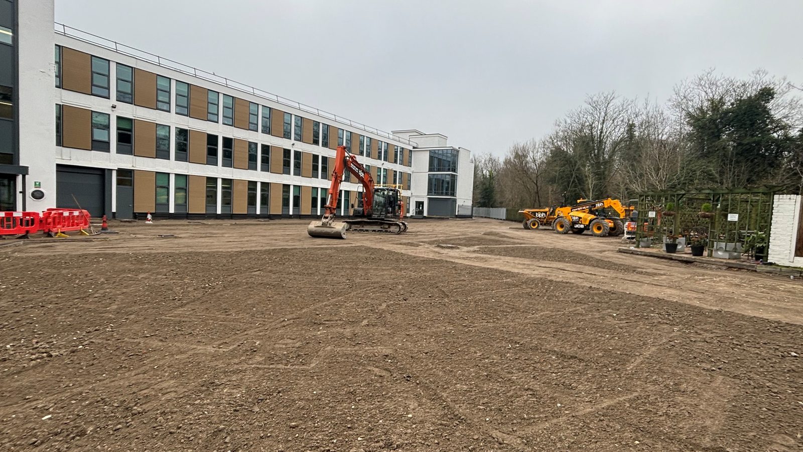 New baseworks and a tracked excavator beside a commercial building during car park enabling works in Sutton.