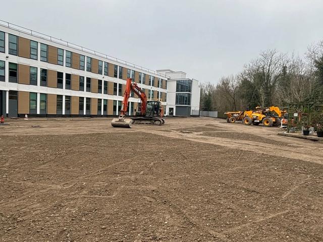 New baseworks and a tracked excavator beside a commercial building during car park enabling works in Sutton.