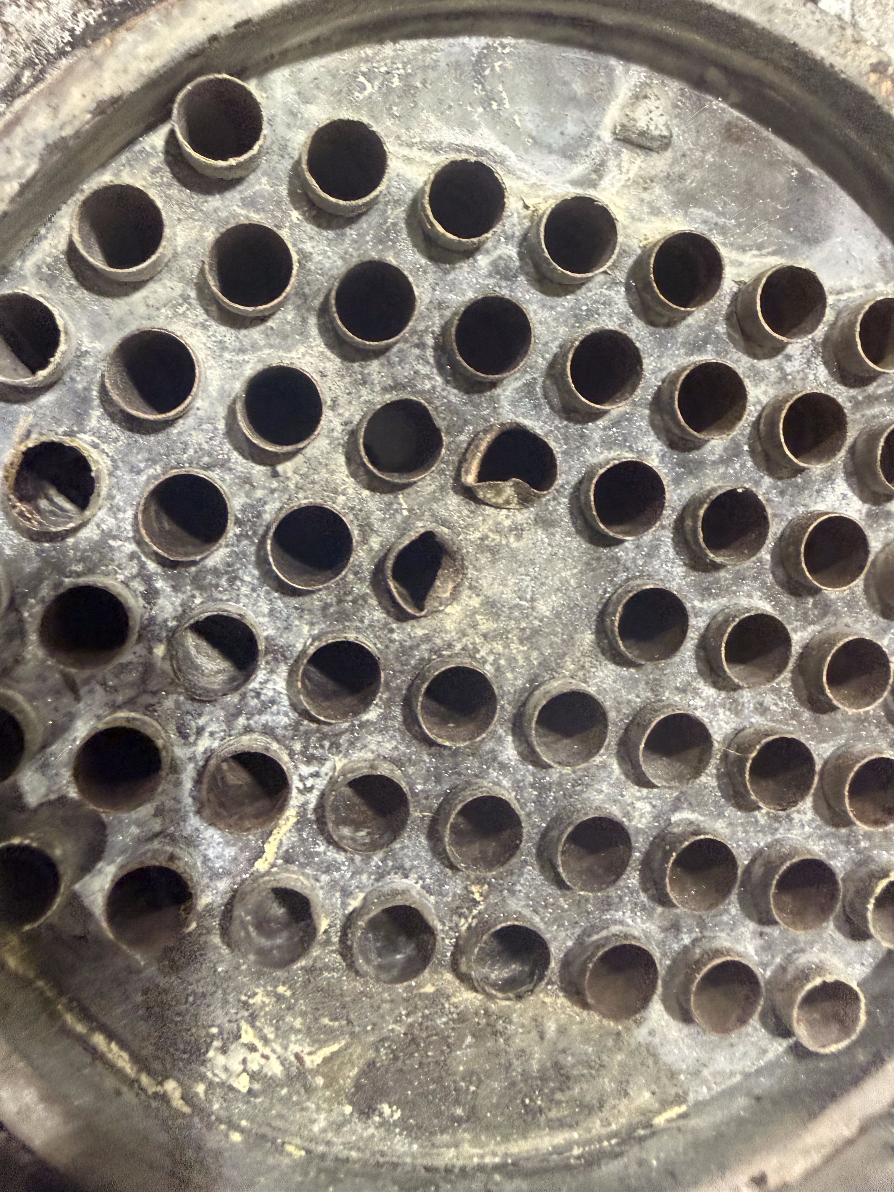 Close-up of the aftercooler's copper tube bundle from the end, showing two cracked tube openings among the surrounding intact, round ones.