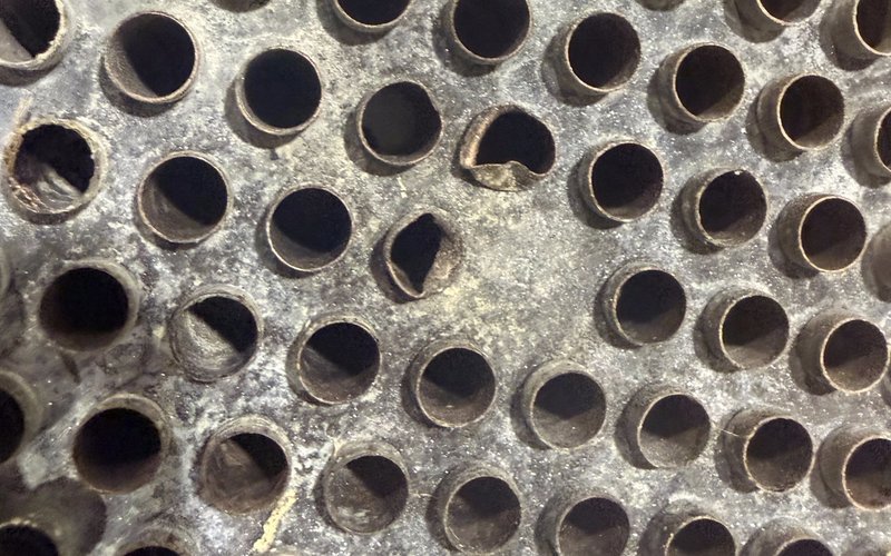 Close-up of the aftercooler's copper tube bundle from the end, showing two cracked tube openings among the surrounding intact, round ones.
