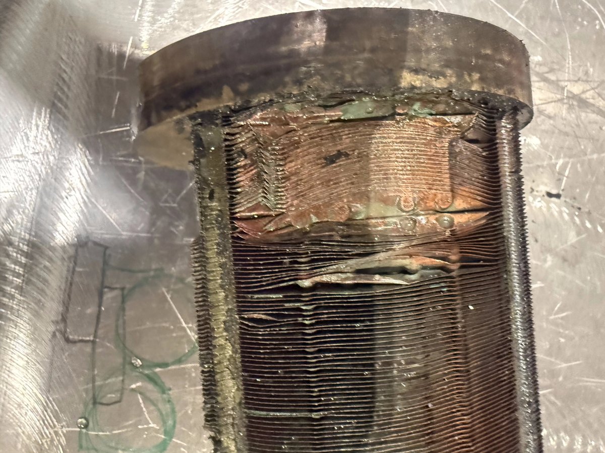 Close-up of the aftercooler housing, deteriorated and sitting out of alignment against the copper tube stack.