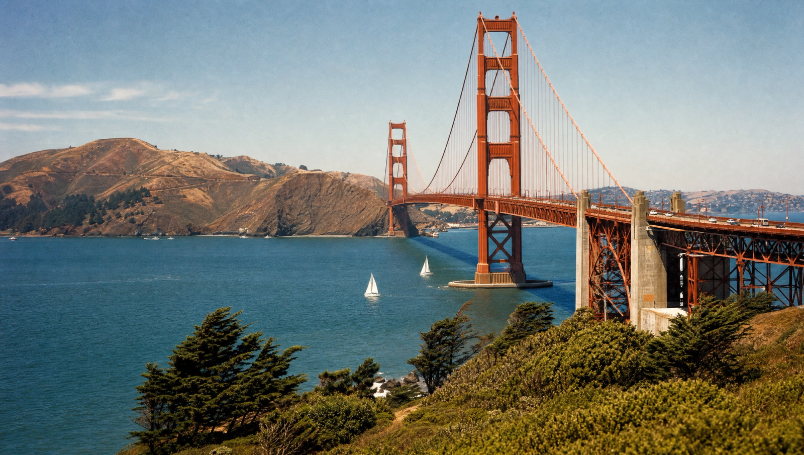 Golden Gate Bridge in San Francisco seen from a hillside, with sailboats on the bay. A classic American travel icon.