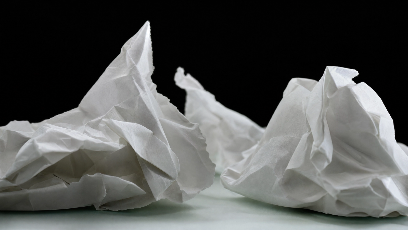 Crumpled white paper folded into mountain-like peaks against a black background a minimalist visual metaphor for tension or complexity.