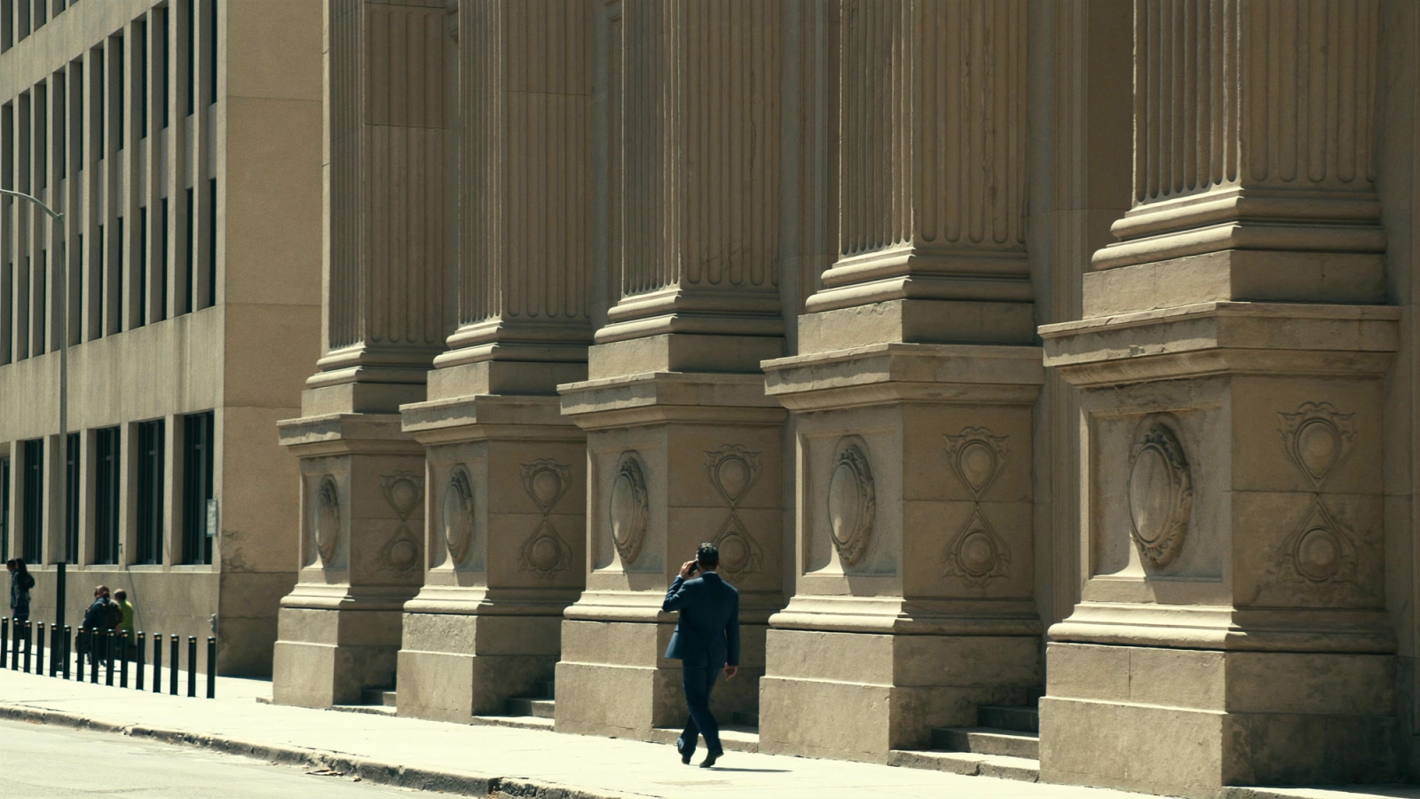 Businessman in a dark suit on the phone walking past a large stone building, symbolizing the PKV vs GKV choice for high earners.