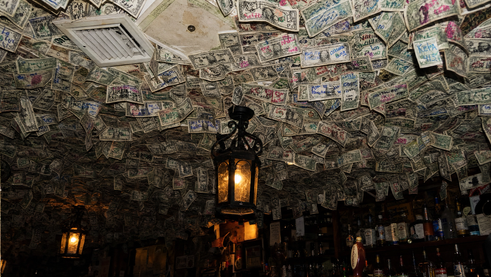 A dollar-bill-covered dive bar ceiling — a cheeky visual metaphor for weighing whether private health insurance is worth it."