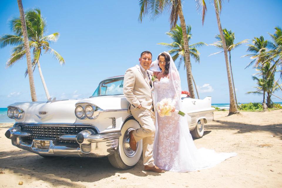 Couple d’elopement à côté d’une voiture ancienne blanche sur une plage bordée de palmiers à Punta Cana