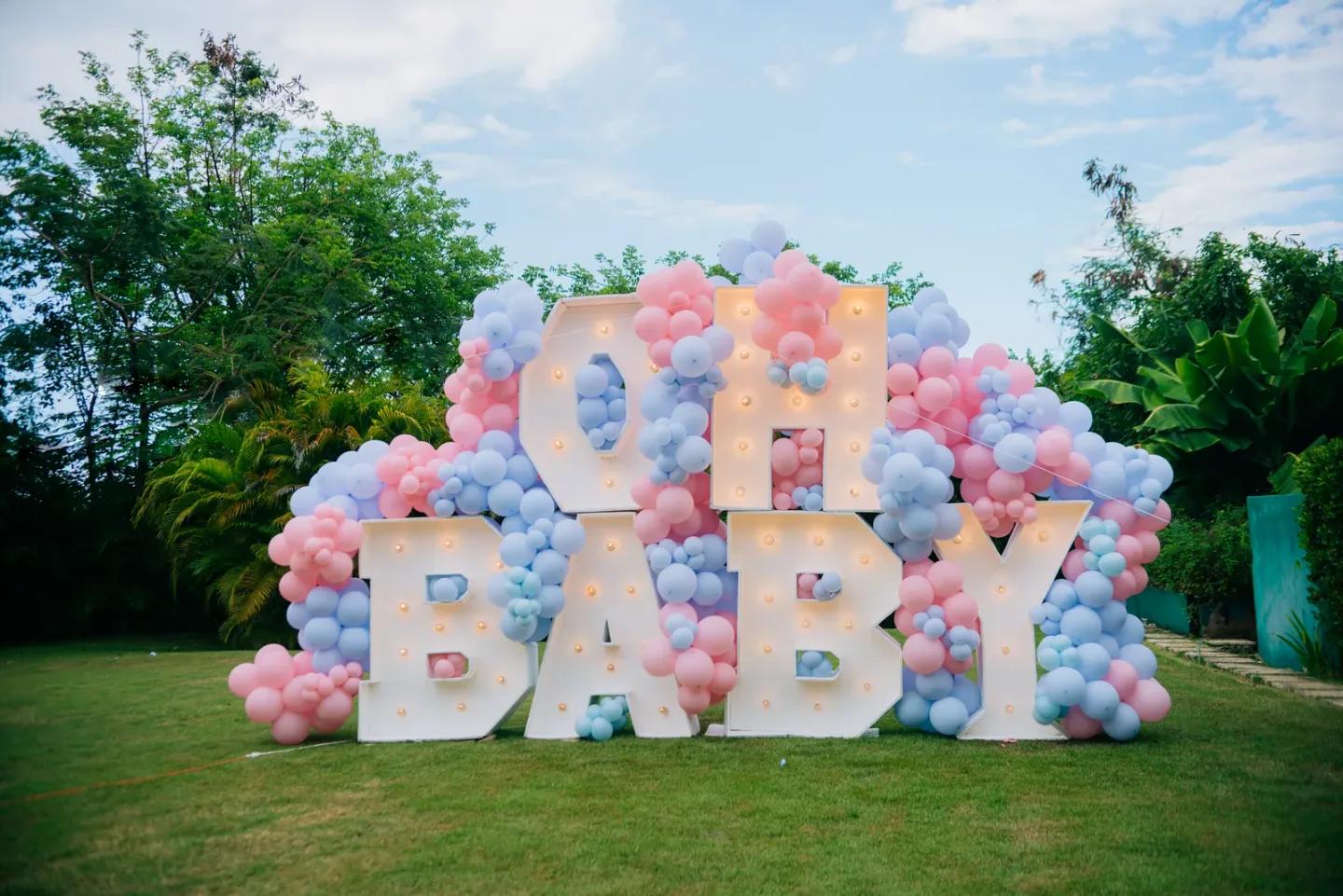 Lettres Oh Baby et ballons pastel dans un décor de révélation au jardin